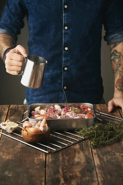 Hombre sostiene olla de salsa de acero por encima de filetes de carne cruda — Foto de Stock