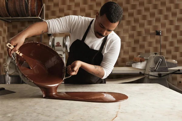 Chef gießt schmackhafte geschmolzene Schokolade aus einem Topf auf den Tisch — Stockfoto
