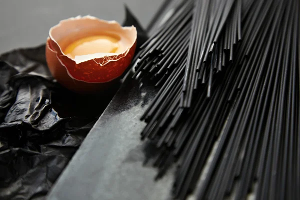 Black spaghetti on craft paper near broken raw egg — Stock Photo, Image