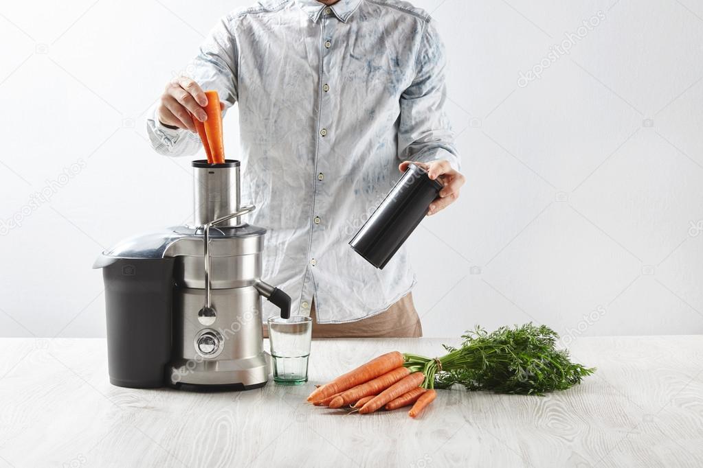 Man puts carrots inside metallic professional juicer — Stock Photo