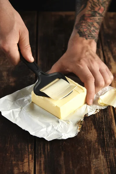 Las manos usan un cuchillo especial para cortar una rebanada fina de mantequilla —  Fotos de Stock