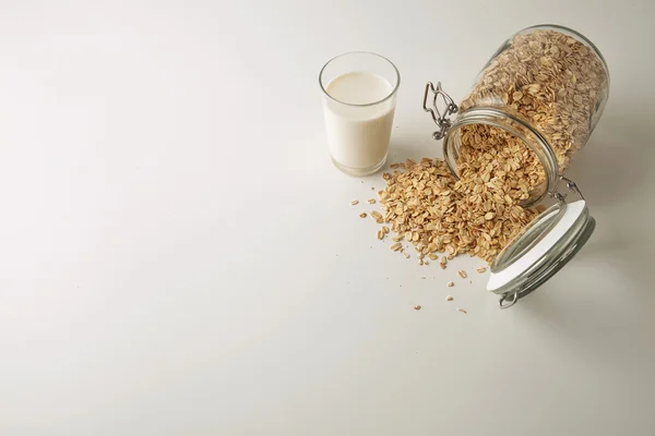 Glass with organic milk near opened jar with oats — Stock Photo, Image