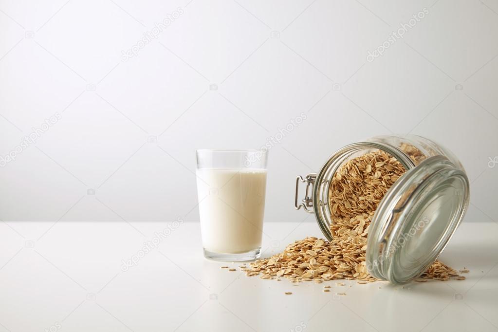 glass with organic milk  near opened jar with oats