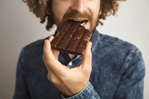Homem morde bar de chocolate saboroso — Fotografia de Stock