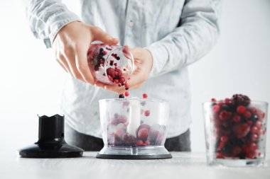 Man adds frozen berries to focused blender pot  clipart