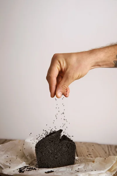 Tätowierte Hand gießt Samen aufs Brot — Stockfoto