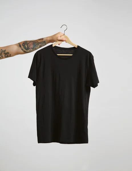 Mão segura pendurar com t-shirt preta — Fotografia de Stock