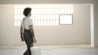 adam beyaz boya ve fırça rulo ile kova getiriyor