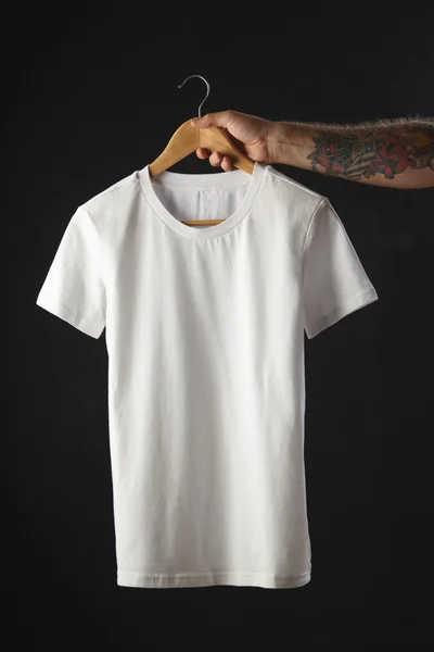 Getatoeëerde hand houdt wit blank t-shirt — Stockfoto