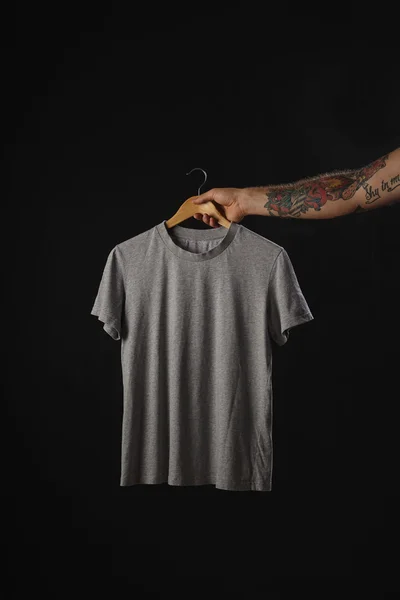 Tatuado mano sostiene gris en blanco camiseta —  Fotos de Stock