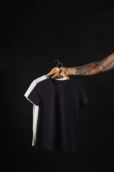 Tatuerade handen rymmer svart och vitt t-shirts — Stockfoto