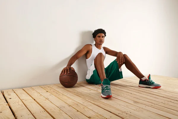 Jugador sentado en el suelo y la mano descansando en el baloncesto — Foto de Stock