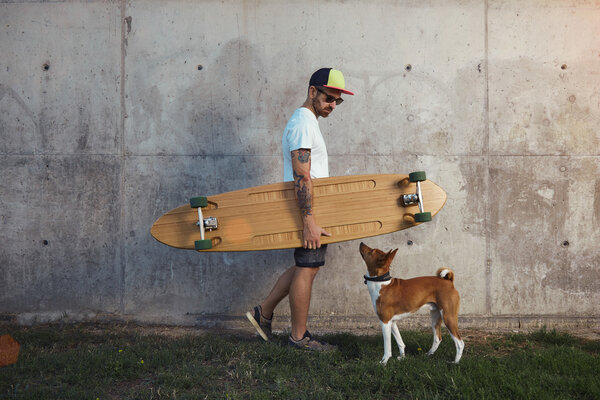 Longboarder with dog next to gray concrete wall