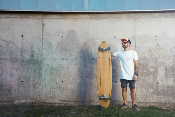 Tatuoitu mies seisoo puinen longboard — kuvapankkivalokuva