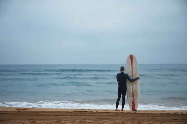 Vanha surffaaja kanssa surffilauta pysyy yksin rannalla — kuvapankkivalokuva