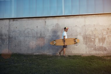 Beton bir duvarın yanında longboard ile Dövmeli adam