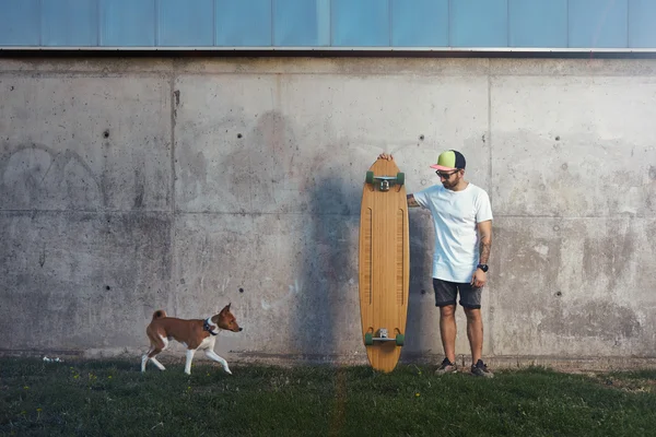 Longboarder basenji koira vieressä harmaa betoniseinä — kuvapankkivalokuva