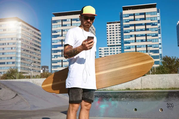 Skater sostiene longboard y mira el teléfono inteligente — Foto de Stock