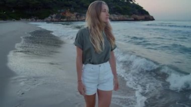 Genç bir kadın sahilde suyun kenarında yürüyor.