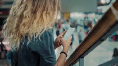 Genç kadın meşgul tren istasyonunda akıllı telefon kullanıyor.