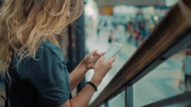 Genç kadın meşgul tren istasyonunda akıllı telefon kullanıyor.