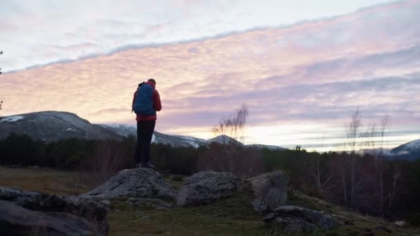 Hombre con mochila mira el atardecer sobre la montaña — Vídeos de Stock