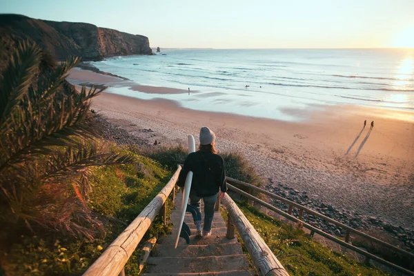 Mujer joven surfista caminar hasta la playa al amanecer —  Fotos de Stock