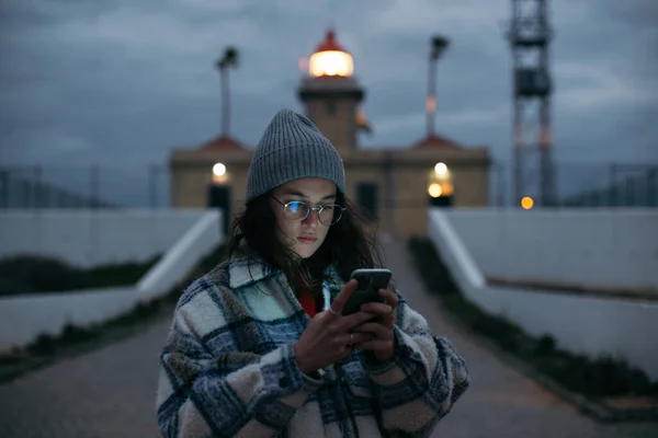 Молода жінка дивиться на смартфон у сутінковому світлі — стокове фото