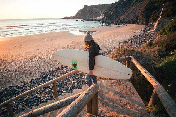 Nuori nainen surffaaja kävelee rannalle auringonnousun aikaan kuvapankin valokuva