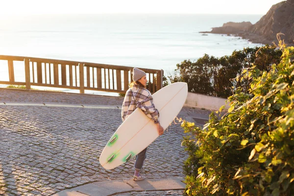 Nuori nainen surffaaja kävelee rannalle auringonnousun aikaan — kuvapankkivalokuva