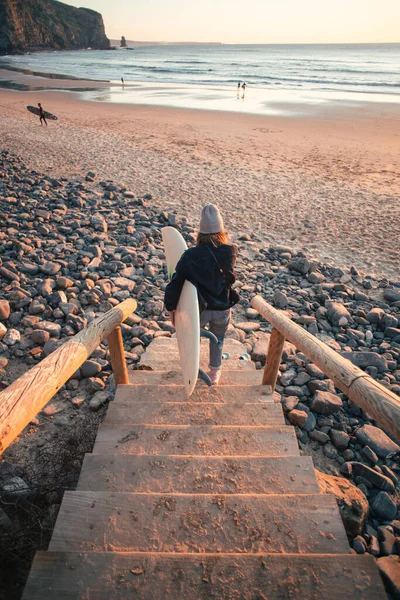 Νεαρή γυναίκα σέρφερ κατεβαίνει στην παραλία την ανατολή του ηλίου — Φωτογραφία Αρχείου