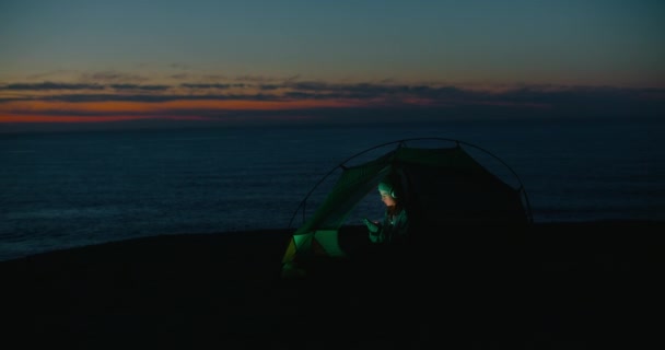 Magányos fiatal nő néz telefon kemping sátor — Stock videók