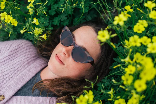 Millennial woman lay in flowers in spring grass
