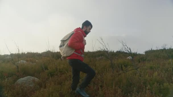 風の強い日に赤いパフィージャケットハイキングの男 — ストック動画