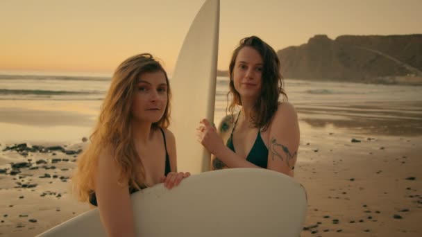 Two female surfers at sunset beach look at camera — Stock Video