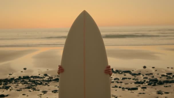 Młoda kobieta z deską surfingową na epickiej plaży zachody słońca — Wideo stockowe