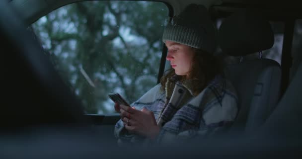 Vrouw zit in auto, scherm verlicht gezicht met telefoon — Stockvideo