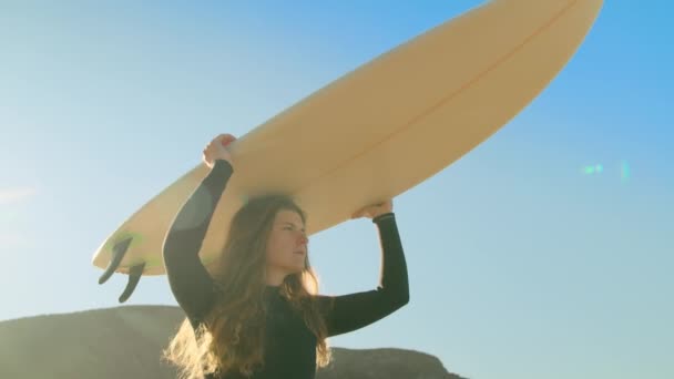 Νεαρή γυναίκα σέρφερ μεταφέρουν ιστιοσανίδα στην παραλία — Αρχείο Βίντεο