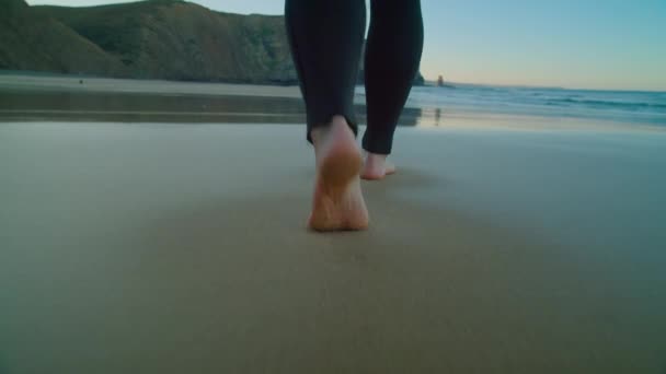 Fényképezőgép követi mezítláb szörfös búvárruhában a strandon — Stock videók