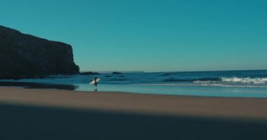 Efsanevi sahilde sörfçü bir kadın figürü.