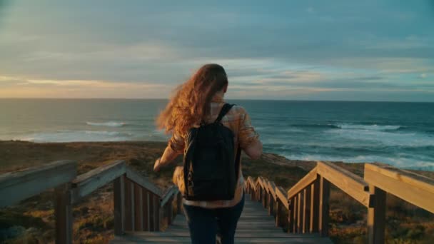 若い女性旅行者は日没のビーチで海に走ります — ストック動画
