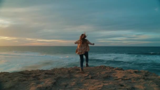 Szczęśliwa wolna kobieta biegnie nad ocean o zachodzie słońca — Wideo stockowe