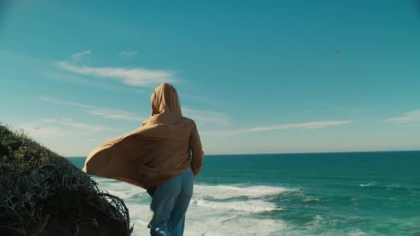 Woman stand on edge of ocean cliff with phone — Stockvideo