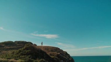 Kadın elinde telefonla okyanus uçurumunun kenarında duruyor.