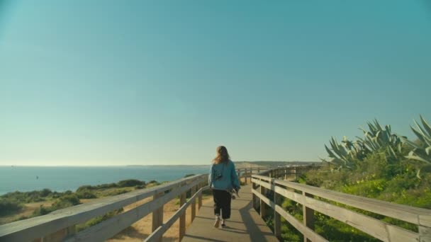 Young woman walk with longboard on boardwalk — Stock Video