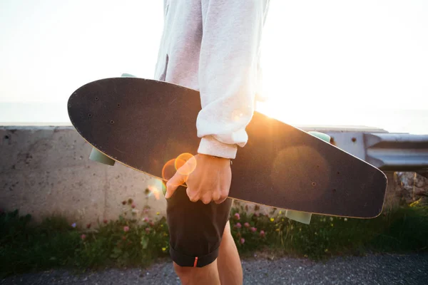 Nuori hipsteri kantaa longboardia auringonlaskun aikaan. — kuvapankkivalokuva