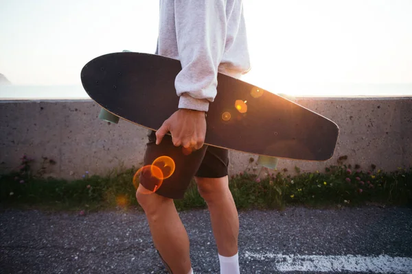 Jovem hipster carrega longboard ao pôr do sol — Fotografia de Stock
