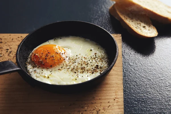 Жареное яйцо в маленькой кастрюле с ломтиками хлеба на завтрак — стоковое фото