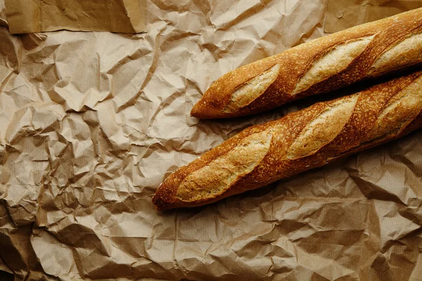 Two freshly baked baguettes in corner on craft paper