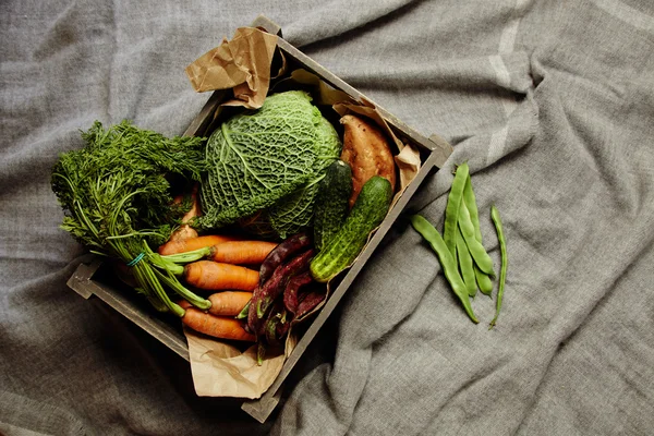 Colheita de legumes em caixa de madeira com papel artesanal em pano — Fotografia de Stock